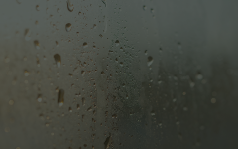 Close-up of water droplets and heavy condensation on a foggy glass window.