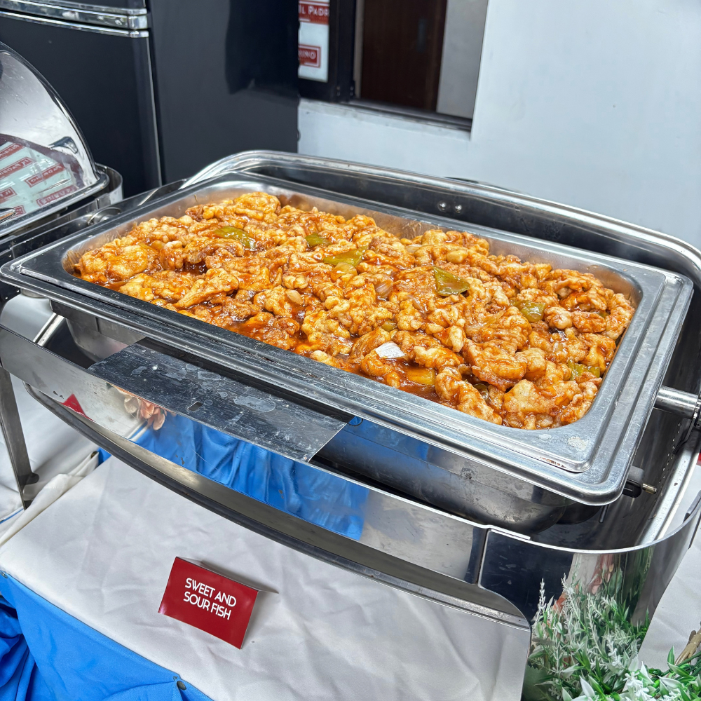 A stainless steel catering chafing dish filled with sweet and sour fish.
